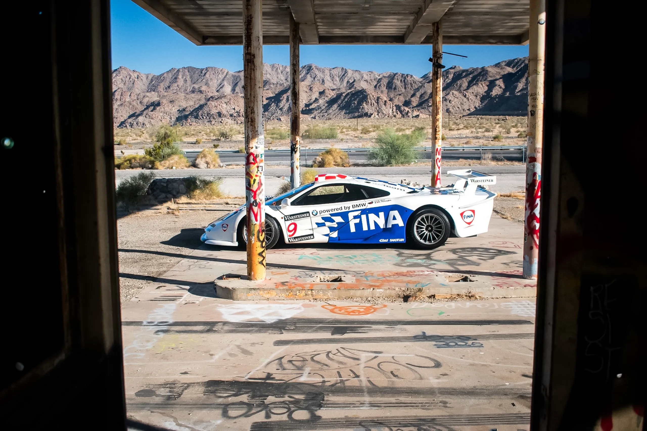 White and blue McLaren F1 GTR in FINA livery, posed at an abandoned desert gas station